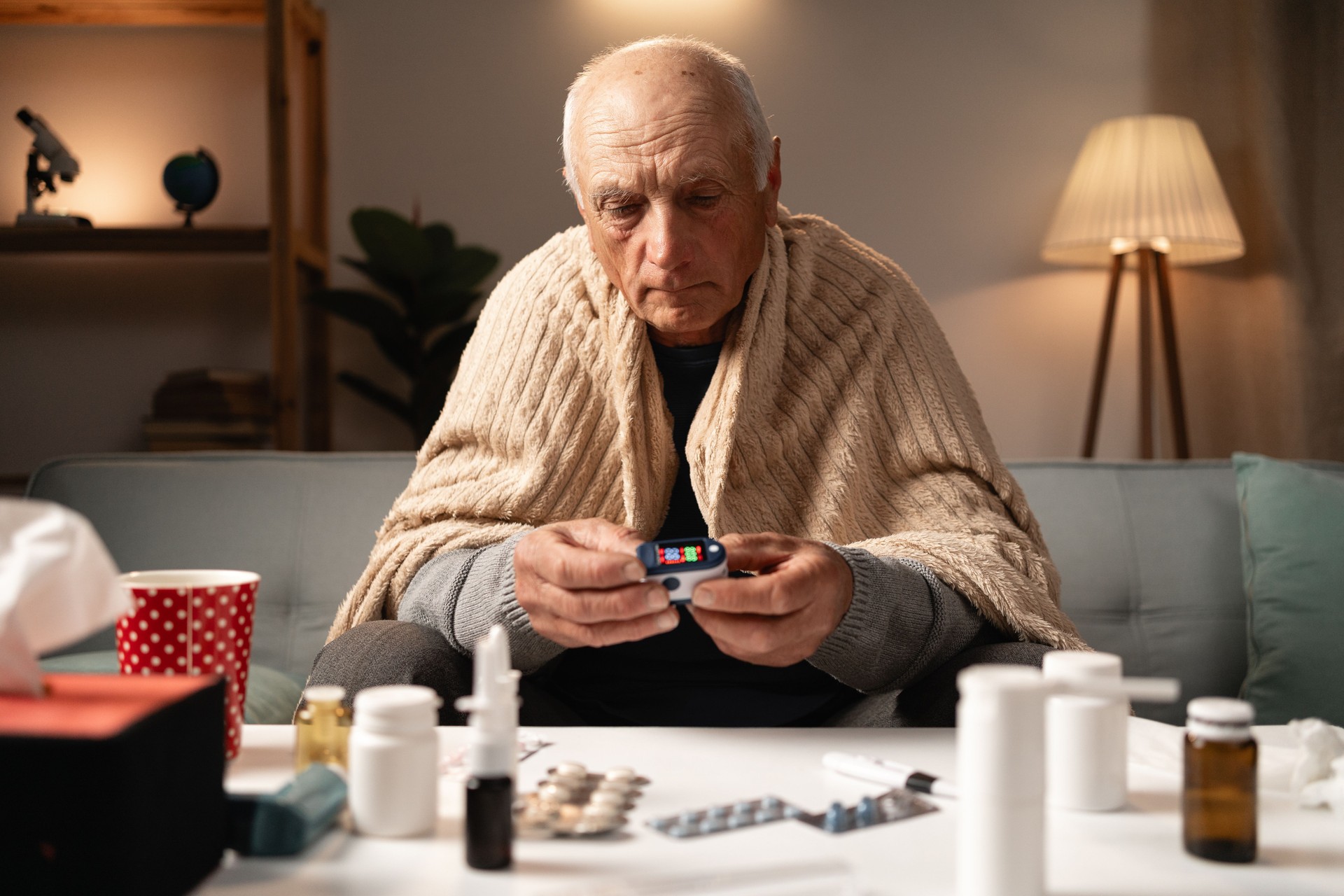 Homme âgé utilisant un oxymètre de pouls pour surveiller la santé à la maison, entouré de médicaments